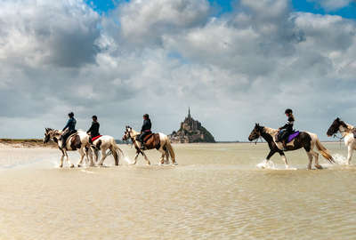 Horses and riders walking in the Ocean by Mt St Michel