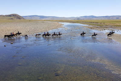 Riders crossing a river on horseback in mongolia