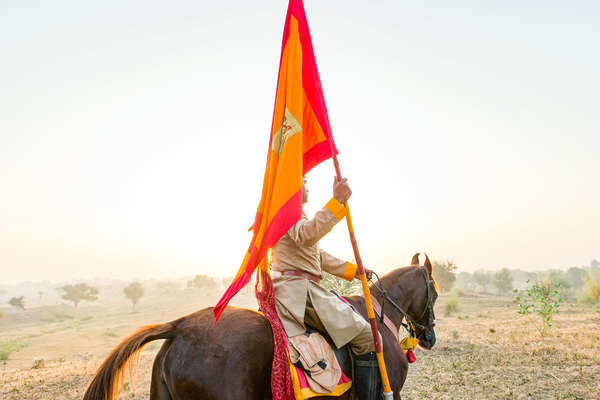 Indian riding carrying a flag and on  horseback
