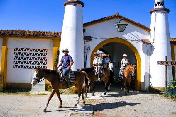 Riders riding out of an hacienda in Portugal under blue skies