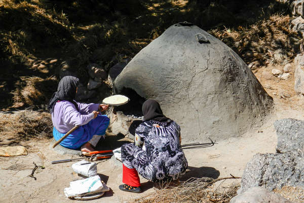 Two Moroccan women preparing food in a clay oven