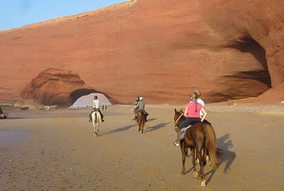 A group of riders riding on the beach by the ocean