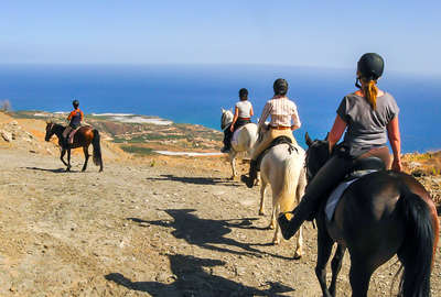 Horseback riders riding on cliffs next to the sea