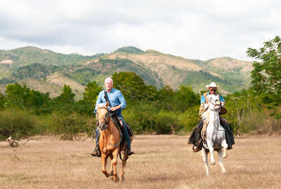 Two riders galloping along a field in Cuba