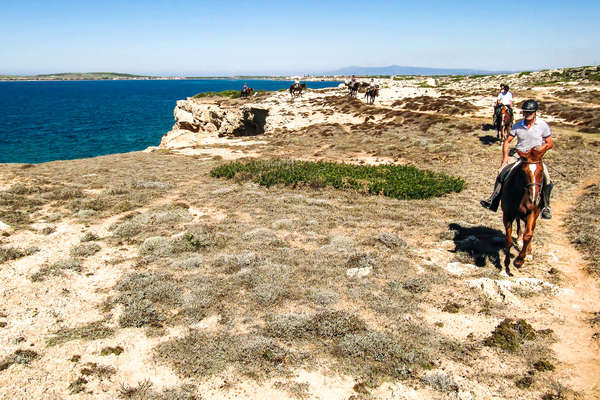 Horseback riders following a cliff path with views of the Mediterranean