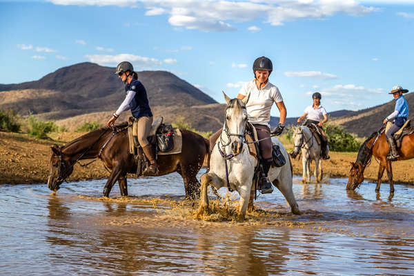 Horseback riders with horses in a lake at Okapuka safaris in Namibia