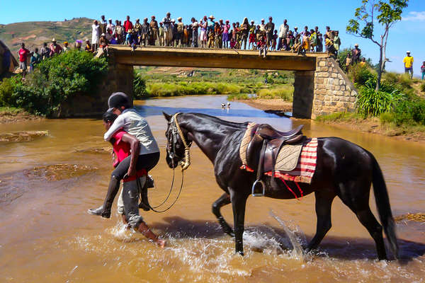 Man carrying a rider and guiding the horse through a river in Madagascar