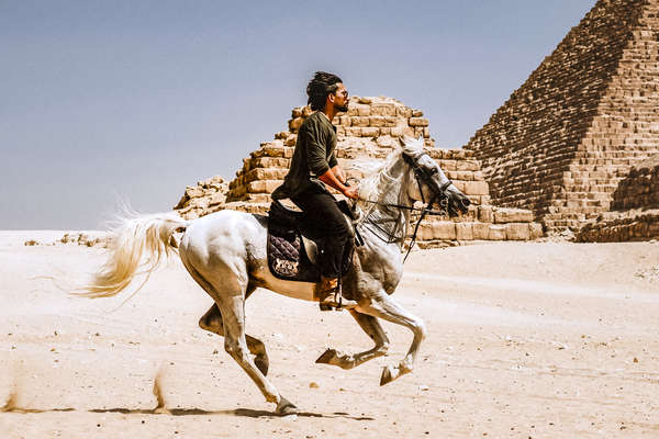 Rider cantering alongside pyraminds in Egypt