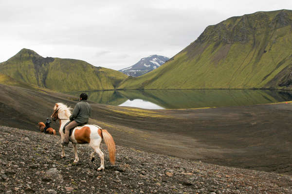 Rider on horseback riding alongside a lake