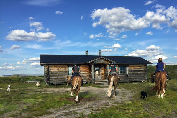 Riders arriving to a rustic cabin on horseback