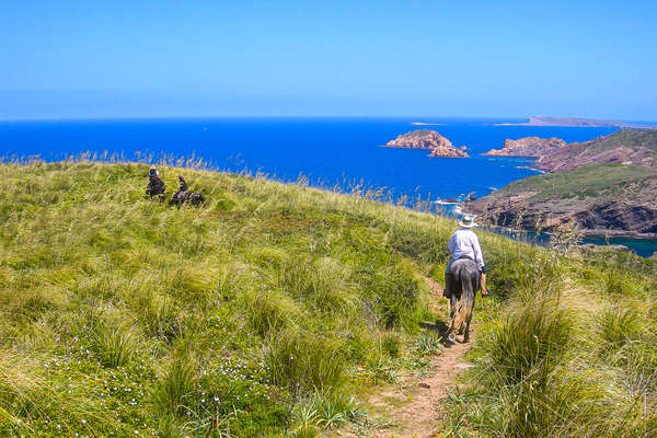 Riders on horseback in Menorca with views of the Mediterranean