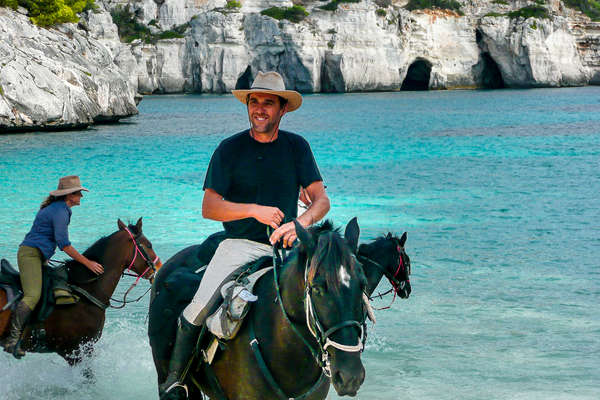 Riders riding into the sea with their horses in Spain