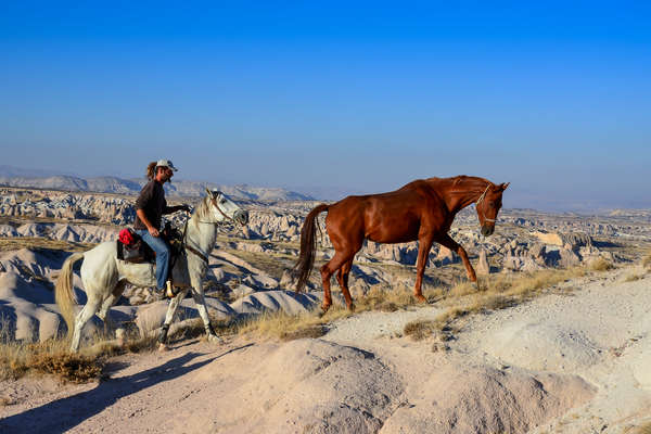 Trail guide leading his horse and loose horse in Cappadocia