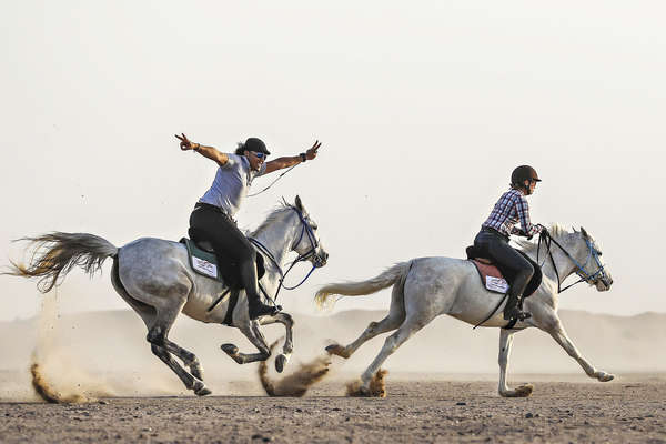 Two riders galloping along a desert in Egypt