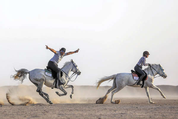 Two riders galloping along a desert in Egypt