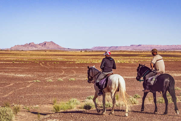 Two riders riding across a Saharian plateau in Morocco