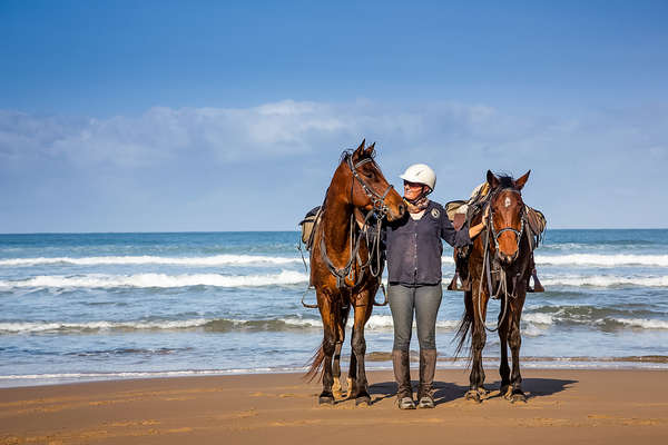 Woman holding two horses on a beach in South Africa